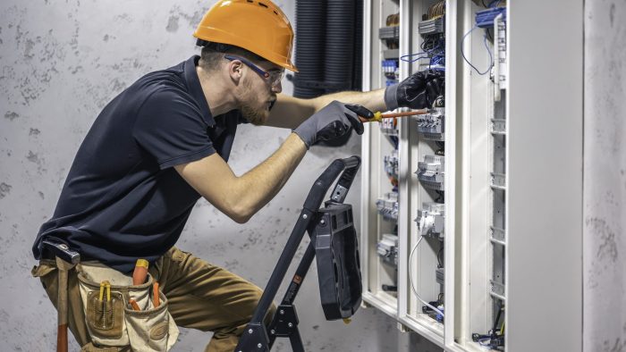 A male electrician works in a switchboard with an electrical connecting cable.